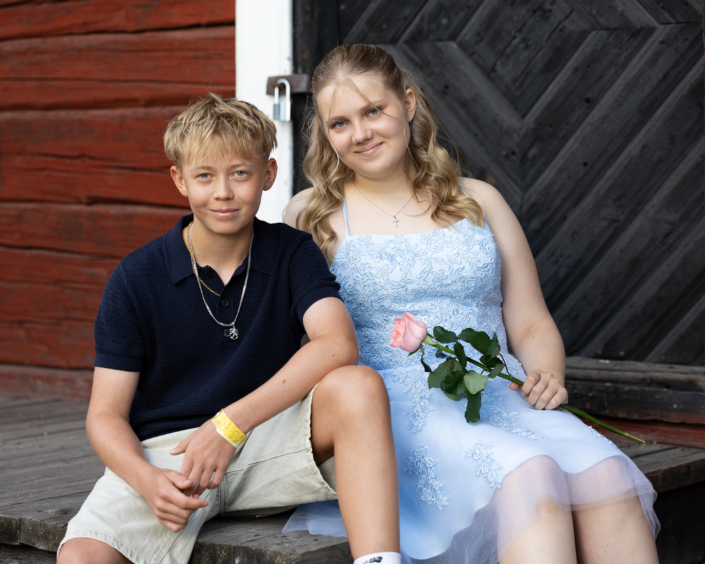 Rippikuvaus Sisarukset rippikuvauksessa ulkona puuoven edessä. Siblings during a confirmation photoshoot outdoors in front of a wooden door.